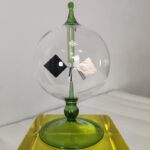 Balancier d'horloge en verre avec éléments métalliques et décoratifs.