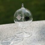 Boule de verre transparente suspendue avec support en métal, utilisée pour des expériences scientifiques ou comme décoration de style scientifique.