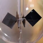 Pendentif scientifique en verre avec aimant et cube noir suspendu, illustrant une expérience de physique ou de chimie. Parfait pour la décoration ou la collection d'objets scientifiques.