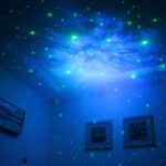 Étoiles phosphorescentes vertes et bleues projetées sur le plafond et les murs d'une pièce sombre, créant une ambiance cosmique et relaxante.