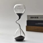 Sablier de laboratoire en verre avec sable noir, symbole du temps et de la science, parfait pour la décoration de bureau ou d'étagère, alliant esthétique et thématique scientifique.
