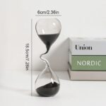 Sablier décoratif en verre transparent avec sable noir, mesurant 18,5 cm de haut et 6 cm de large, idéal pour la décoration intérieure ou comme objet de collection.