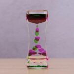 Vase en verre transparent contenant des billes colorées vertes et roses, créant un effet visuel attrayant et moderne. Parfait pour la décoration scientifique ou contemporaine.