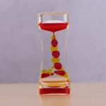 Horloge à sable décorative avec grains rouges et jaunes dans un récipient en verre, idéale pour la décoration scientifique ou éducative.