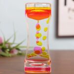 Vase en verre transparent contenant un liquide coloré rose et jaune, avec des bulles décoratives suspendues à l’intérieur, créant un effet visuel attrayant et moderne.