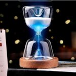 Sablier lumineux en verre avec lumière bleue, posé sur un socle en bois, créant un effet visuel captivant. Parfait pour la décoration de bureau ou comme objet de collection scientifique.