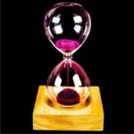 Sablier en verre avec sable rose vibrant, posé sur un socle en bois naturel, illustrant la mesure du temps avec élégance et modernité.