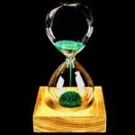Sablier en verre avec boule de mousse verte en suspension, posé sur une base en bois, illustrant un objet scientifique décoratif et original.