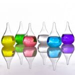 Vases de laboratoire en verre avec liquides colorés jaune, vert, rose, transparent, bleu et violet, disposés en ligne avec leur reflet sur une surface lisse.