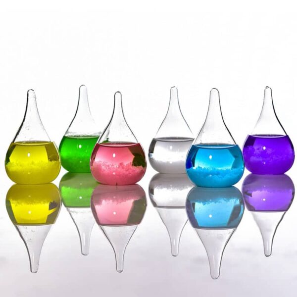 Vases de laboratoire en verre avec liquides colorés jaune, vert, rose, transparent, bleu et violet, disposés en ligne avec leur reflet sur une surface lisse.