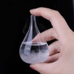 Pipette en verre contenant un liquide vaporisé, tenue par une main contre un fond noir, illustrant une expérience scientifique ou une démonstration de laboratoire.