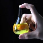 Petite fiole de laboratoire contenant un liquide jaune fluorescent, tenue par une main contre un fond noir, illustrant la science et la recherche.