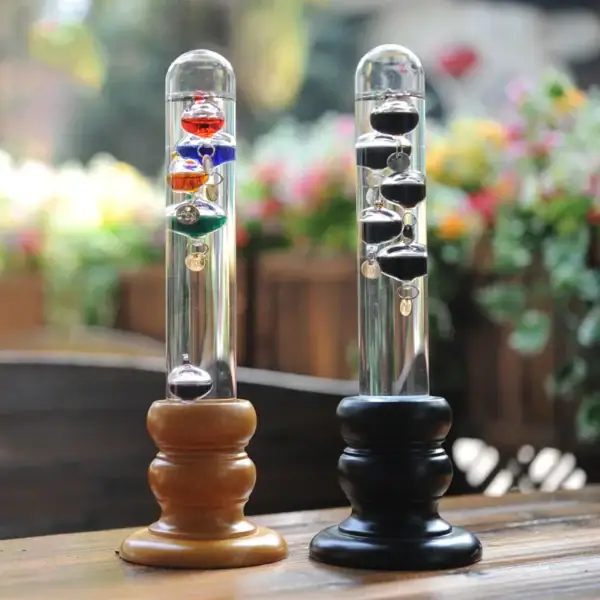 Balançoire de Newton avec billes colorées suspendues, illustrant la loi de la conservation de la quantité de mouvement, sur une table en bois avec un fond flou de fleurs.