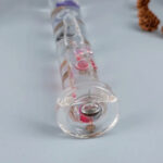 Pipette en verre contenant un liquide rose, utilisée pour des expériences scientifiques ou éducatives, posée sur une surface blanche.