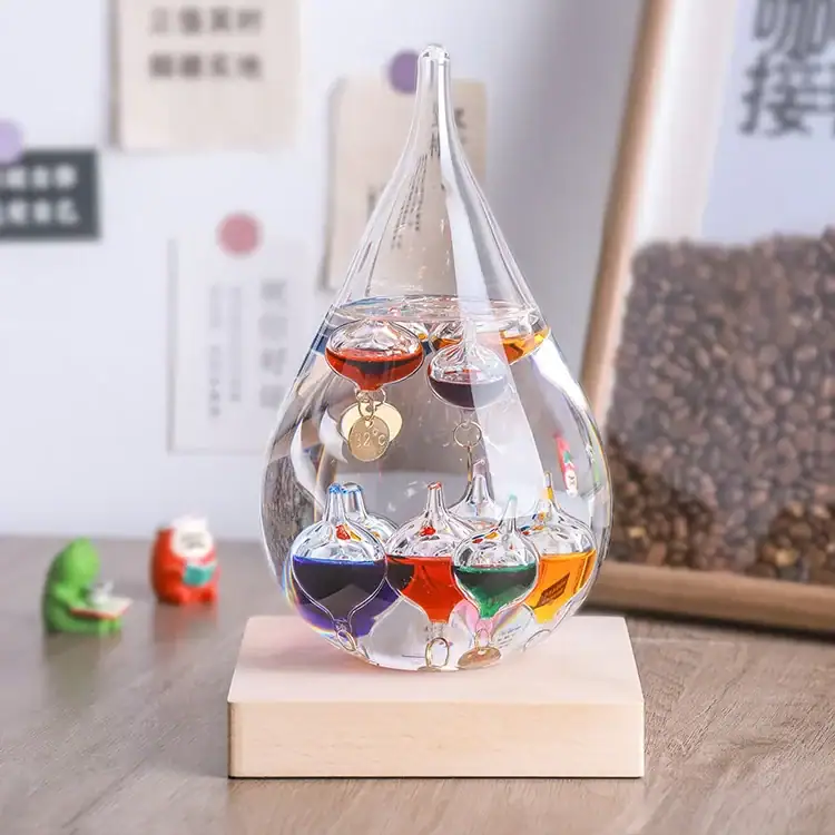 Pendentif scientifique en verre transparent contenant des liquides colorés suspendus, présenté sur une base en bois, décoratif et éducatif.