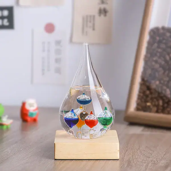 Pipette en verre contenant des liquides colorés (bleu, rouge, vert) sur un socle en bois, dans un environnement de bureau ou de laboratoire avec des notes et des objets scientifiques en arrière-plan.