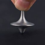 Petite pétrule de Foucault en métal brillant, tenue par un doigt, illustrant la rotation pour démonstration scientifique.