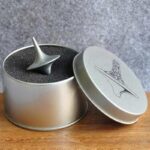 Torpille de bateau en métal dans une boîte cadeau ronde avec couvercle illustré d'une silhouette de bateau. Parfait pour décoration ou collection scientifique.