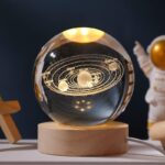 Sphere en cristal représentant le système solaire avec planètes et orbites gravées, posée sur un socle en bois, idéale pour la décoration scientifique et éducative.