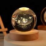 Globe du système solaire lumineux en verre avec planètes et orbites, éclairé pour mettre en valeur les détails, posé sur un socle en bois, idéal pour la décoration scientifique.