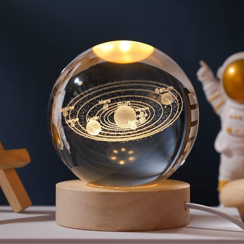 Sphere en cristal représentant le système solaire avec planètes et orbites gravées, posée sur un socle en bois, idéale pour la décoration scientifique et éducative.