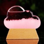 Nuage en verre transparent avec éclairage LED rose, posé sur une base en bois naturel, créant un objet décoratif original et lumineux.