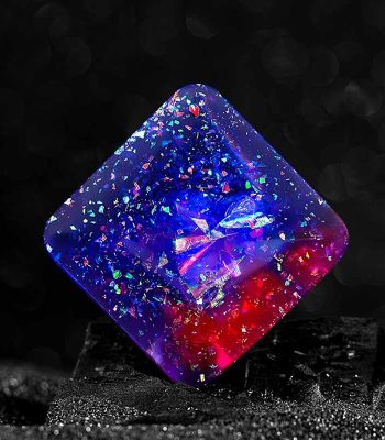 Cube en résine transparent avec des éclats de couleurs fluorescentes, illuminé dans l'obscurité, créant un effet visuel captivant et mystérieux.