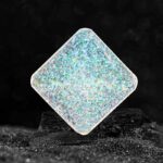 Pendentif en verre holographique carré avec effet iridescent, posé sur une surface noire pour mettre en valeur ses reflets colorés et sa texture brillante.