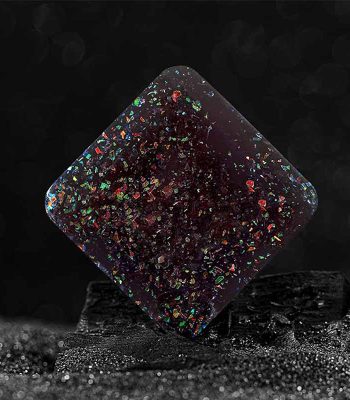 Pendentif en résine transparent avec des éclats holographiques colorés, posé sur une surface noire pour mettre en valeur ses reflets irisés.