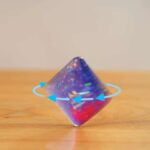 Pyramide en verre transparent avec effets lumineux colorés, posée sur une surface en bois, illustrant un objet scientifique décoratif.
