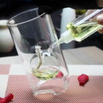 Expérience scientifique avec liquide vert dans un verre en verre, versé à partir d'une pipette, sur une nappe à carreaux rouges et blancs.