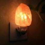 Lampe en sel de l'Himalaya éclairée, branchée à une prise électrique, créant une ambiance chaleureuse et apaisante. Parfaite pour la décoration intérieure ou la relaxation.