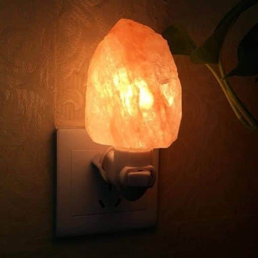 Lampe en sel de l'Himalaya éclairée, branchée à une prise électrique, créant une ambiance chaleureuse et apaisante. Parfaite pour la décoration intérieure ou la relaxation.