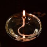 Bougie de laboratoire allumée dans un récipient en verre, avec une flamme vive et une mèche en spirale, sur fond noir.