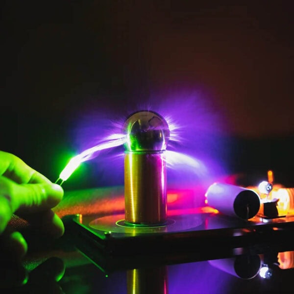 Puce de Tesla générant une décharge électrique colorée avec des effets lumineux violets, verts et bleus, illustrant une expérience scientifique fascinante.