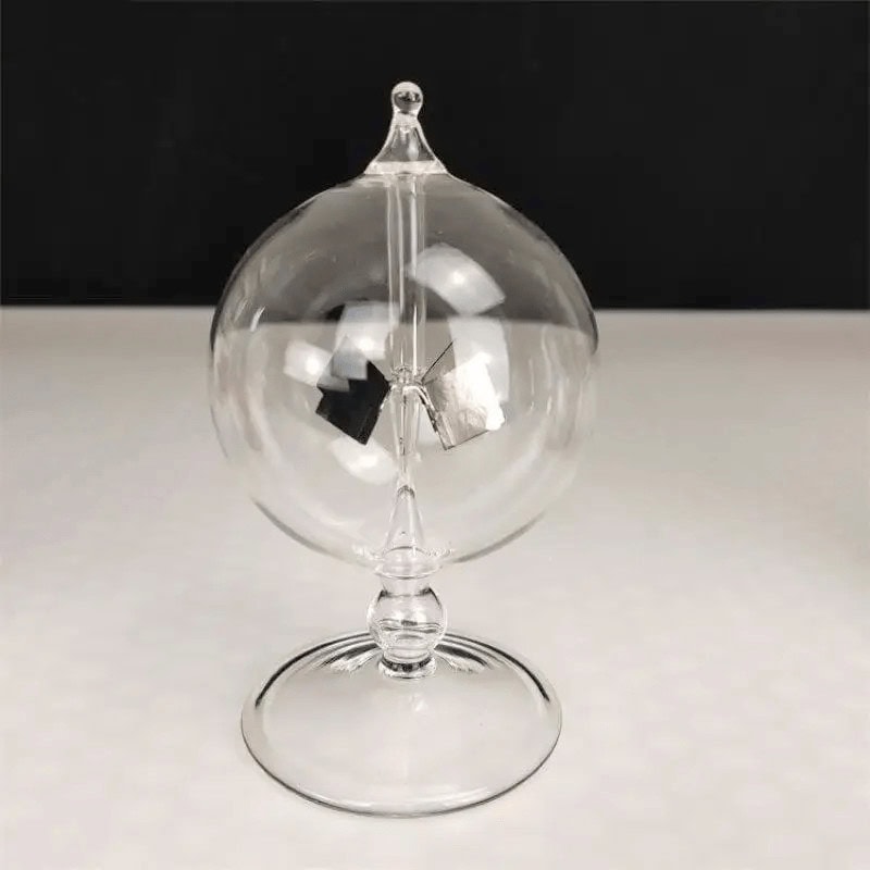 Boule à pendule en verre transparent avec mécanisme suspendu, décor scientifique élégant, sur fond noir et blanc.
