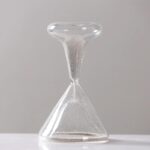 Sablier en verre transparent avec sable blanc fin, symbole du temps qui passe, posé sur une surface blanche avec un fond gris clair.