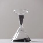 Sablier de laboratoire avec sable noir, symbole du temps et de la science, en verre transparent, posé sur une surface blanche, illustrant la mesure du temps dans un contexte scientifique.