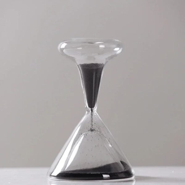 Sablier de laboratoire avec sable noir, symbole du temps et de la science, en verre transparent, posé sur une surface blanche, illustrant la mesure du temps dans un contexte scientifique.