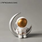 Figurine d'astronaute avec casque doré sur croissant de lune en métal argenté.