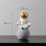 Astronaute en figurine décorative avec casque doré, posée sur une lune en pierre, idéale pour la décoration de bureau ou d'espace scientifique.
