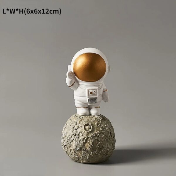 Figurine d'astronaute en plastique blanc avec casque doré brillant, posée sur une petite lune en pierre.