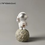 Figurine d'astronaute en décoration, représentant un cosmonautes en combinaison spatiale sur une surface lunaire, idéale pour la décoration thématique scientifique.