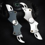 Deux couteaux multifonctions en acier inoxydable avec griffes de préhension, conçus pour la survie et l'aventure, posés sur un sac noir avec un mousqueton.