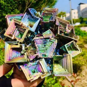Pyramides de cristaux holographiques multicolores, brillantes et géométriques, tenues en main avec un fond naturel en plein air.