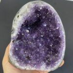 Géode d'améthyste avec cristaux violets brillants, exposée sur fond gris foncé, mettant en valeur la beauté et la structure cristalline de cette pierre précieuse.