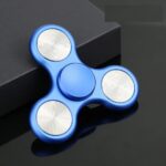 Fidget spinner bleu avec trois branches et roulements en métal, posé sur une surface noire avec un fond sombre.