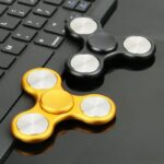 Fidget spinner en métal doré et noir posé sur un clavier d'ordinateur, illustrant un objet de décoration scientifique moderne et tendance.