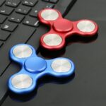 Deux fidget spinners, un rouge et un bleu, posés sur un clavier d'ordinateur, idéaux pour la détente et la concentration.