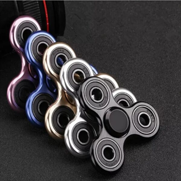 Hand spinner en métal coloré avec trois branches, conçu pour la détente et le divertissement, posé sur une surface sombre.